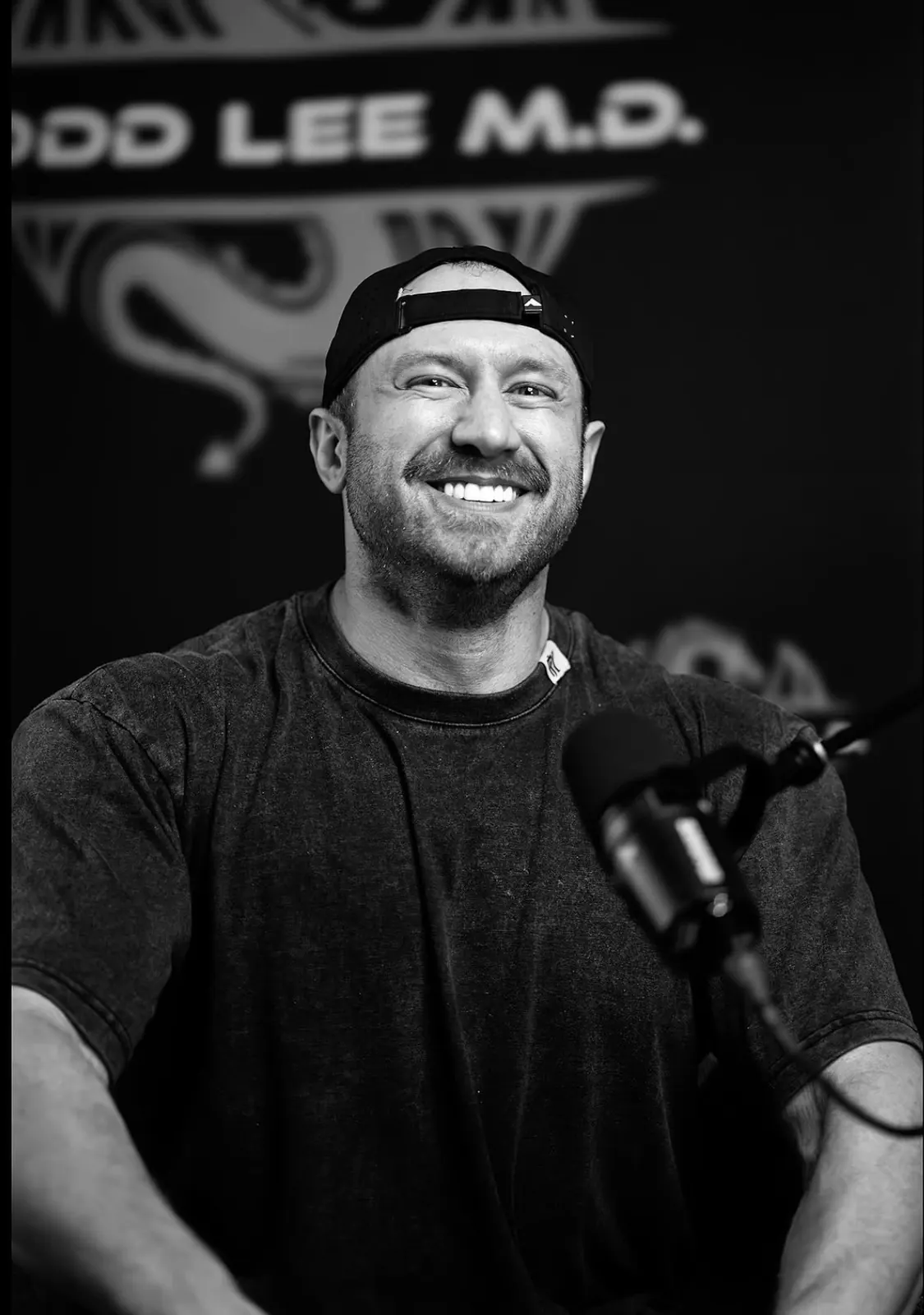 David DeMesquita speaking into a microphone on a podcast, black and white